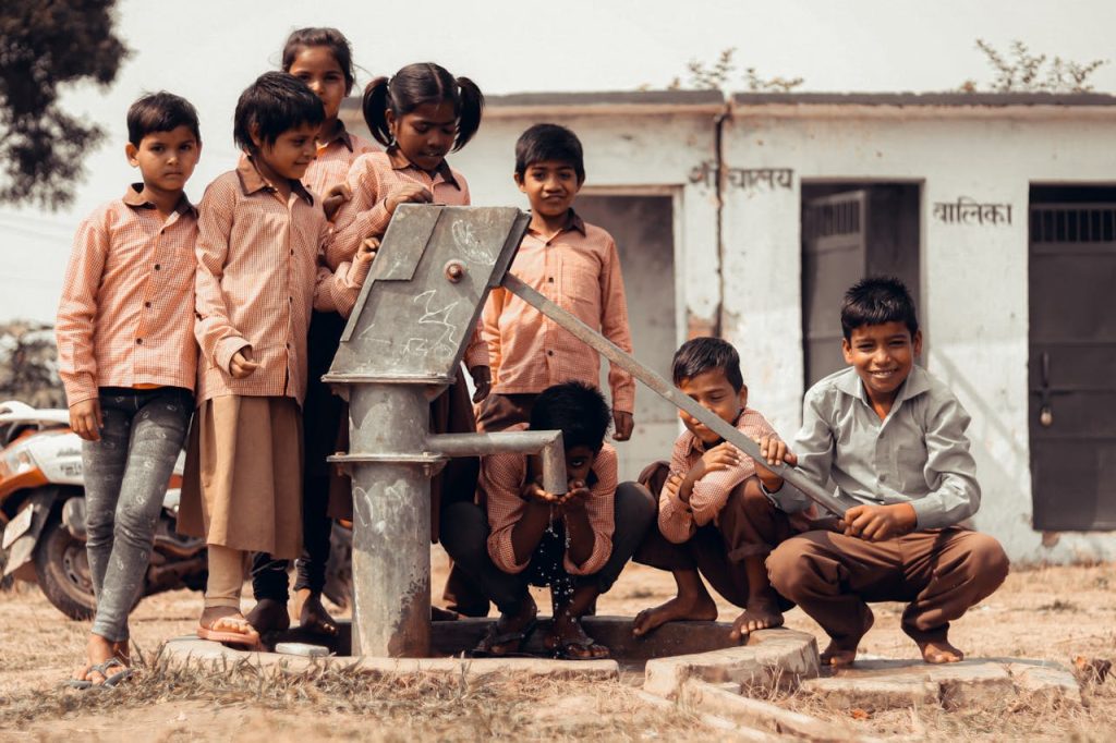 Mastering the First Impression: Your intriguing post title goes here A group of Indian children gather joyfully around a manual water pump outdoors.